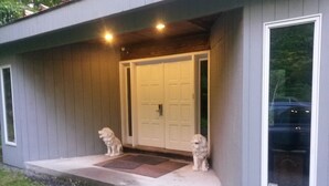 A house with a grey exterior, a front door, and two small dogs on the porch.