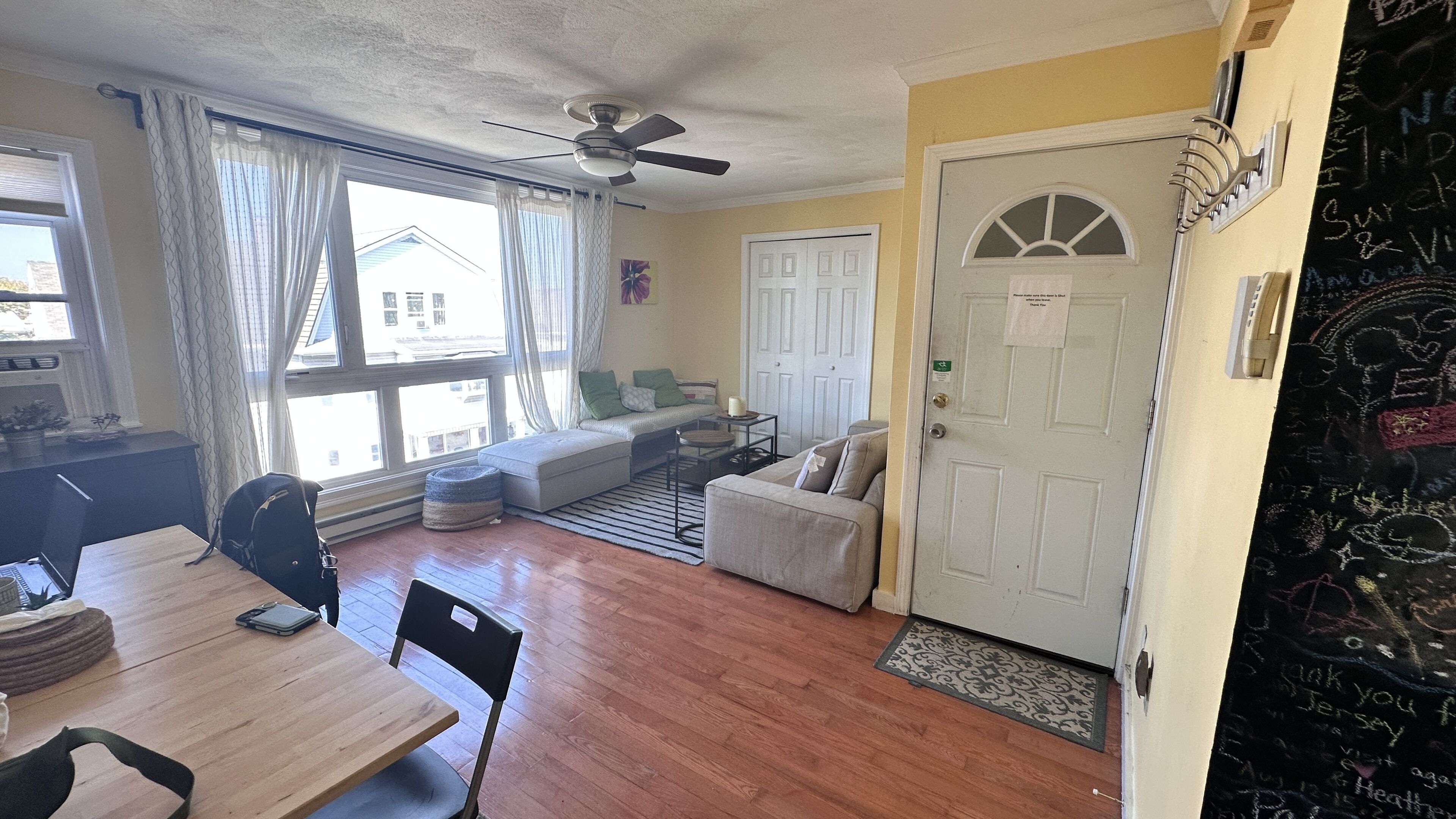 A cozy living room with a wooden dining table, a sofa, and a ceiling fan.