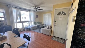 A cozy living room with a wooden dining table, a sofa, and a ceiling fan.