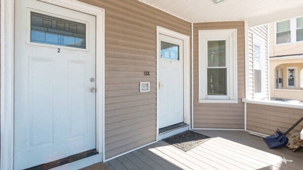 A corner of a house with two white doors, a wooden deck, and a window.