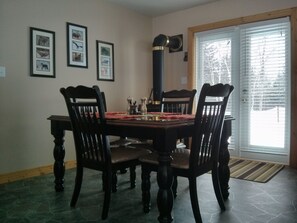 A dining room with a wooden table and four chairs, framed wildlife pictures on the wall, and a large window with blinds.