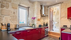 A kitchen with red cabinets, a stone wall, a window with curtains, and a view of the outside.