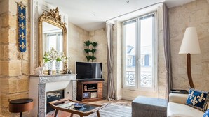 A living room with a fireplace, a television, a sofa, and a large window with curtains.