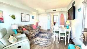 A living room with a sofa, a dining table, and a TV. - 💎ISLAND TIME Dolphin Shack; Gorgeous Direct Oceanfront Balcony King Luxury Bed (Myrtle Beach)
