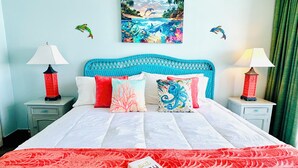 A bed with a coral-patterned bedspread, multiple pillows, and a book titled "eat pray love" on the bed. - 💎ISLAND TIME Dolphin Shack; Gorgeous Direct Oceanfront Balcony King Luxury Bed (Myrtle Beach)
