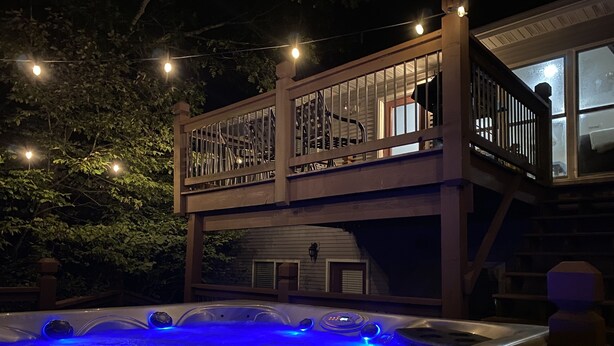 Un bain à remous avec éclairage bleu, une terrasse en bois et un escalier menant à un deuxième niveau.