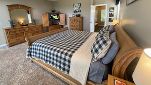 Une chambre à coucher avec un grand lit, une commode en bois, une télévision et une porte donnant sur une autre pièce.