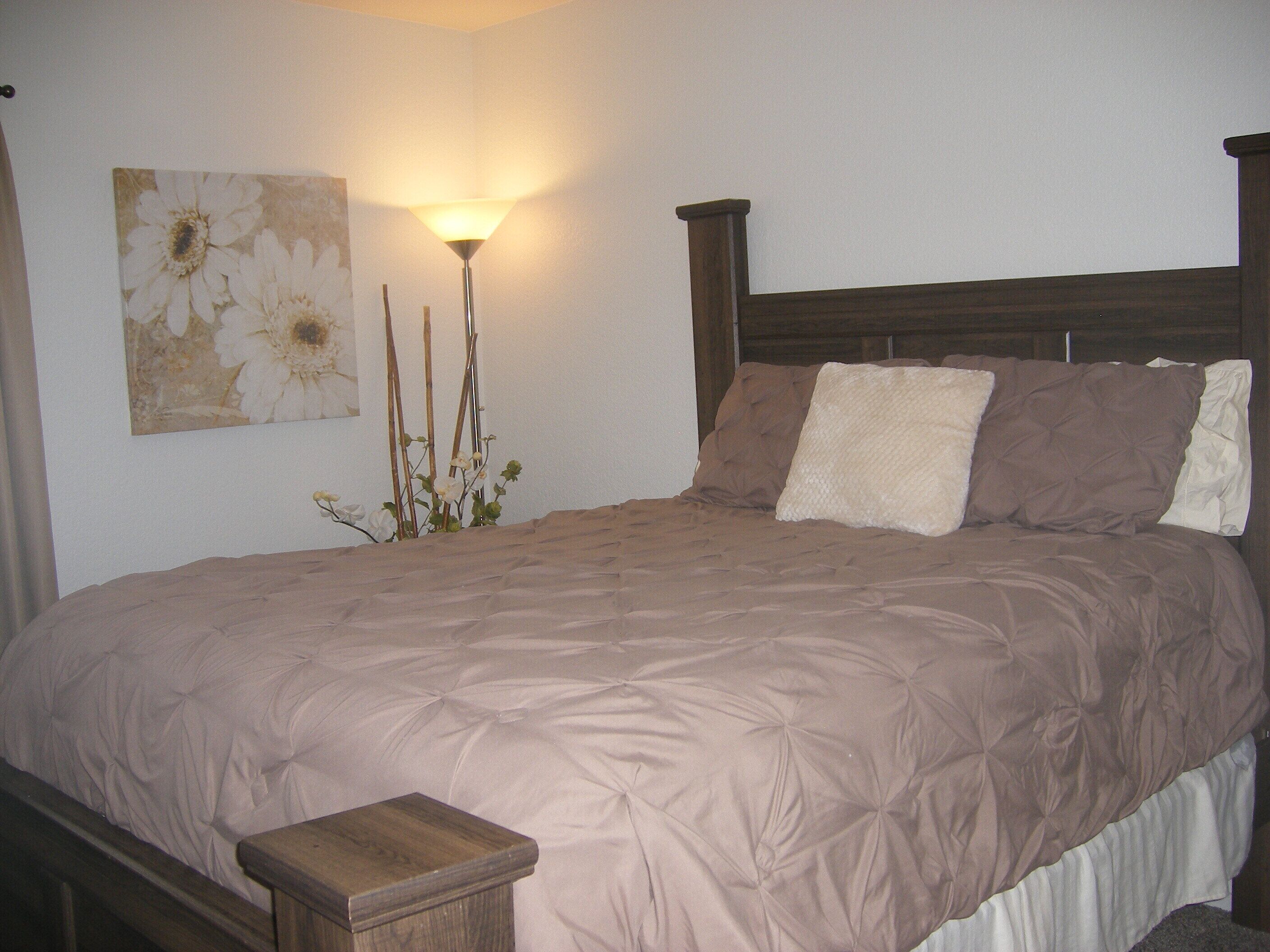 Una cama bien hecha con cabecera, mesita de noche y lámpara de pared.