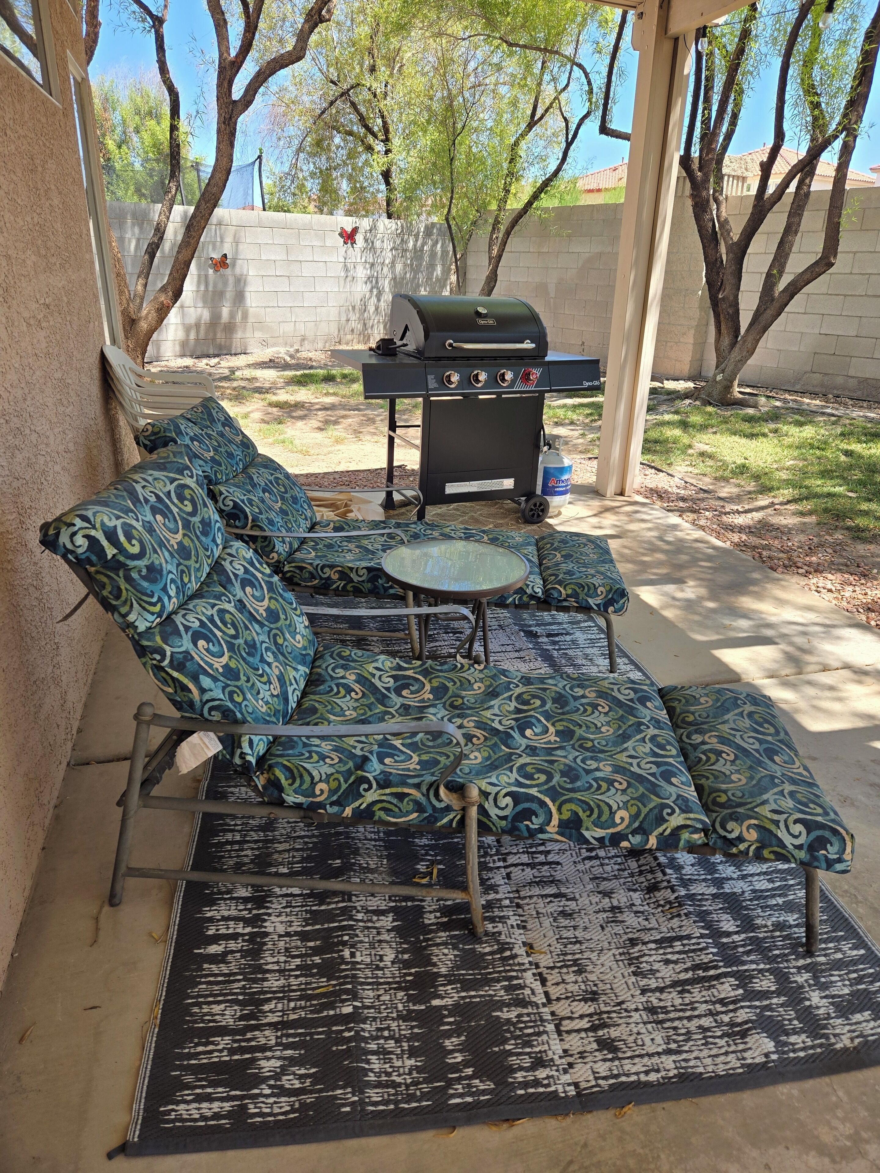 A covered patio with a grill, outdoor seating, and a view of the backyard.