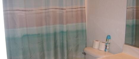 Un baño con cortina de ducha a rayas, un inodoro y un lavamanos con un espejo encima.