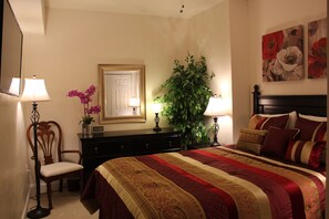 Un dormitorio con una cama grande, un aparador, una silla, un espejo y dos lámparas fijadas a la pared.