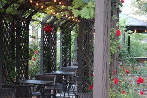 Un patio al aire libre con mesas y sillas, cubierto por una pérgola con luces colgantes.