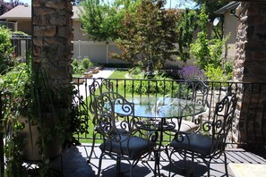 Un patio con una mesa de vidrio y sillas de metal, rodeado de pilares de piedra y una cerca metálica.