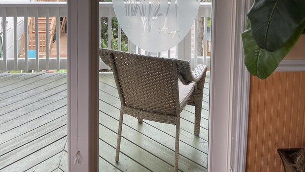 A glass door with a circular frosted design, a wicker chair, and a wooden deck.