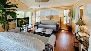 A well-lit living room with a ceiling fan, a television, a sofa, a coffee table, and a large plant.