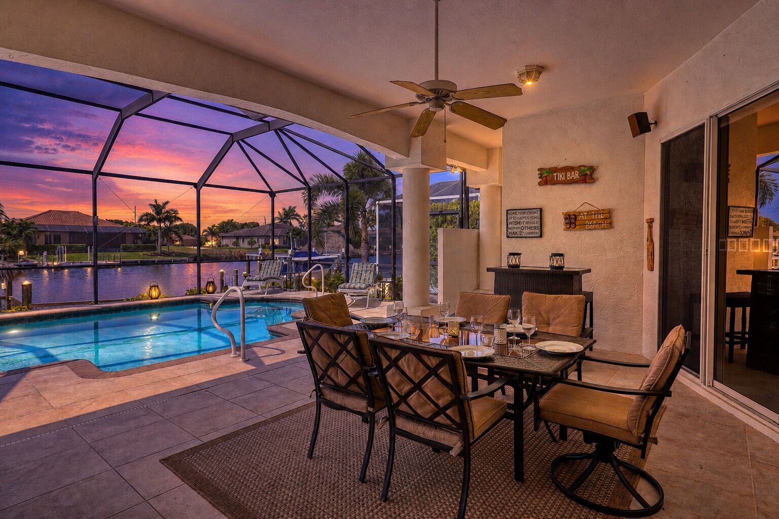 An outdoor pool area with a dining setup, a ceiling fan, and a sign reading 'TIKI BAR'.