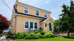 A two-story house with a brick facade, a green door, and a small porch with two chairs. - 5BR w/ 6 King Beds + Hot Tub (Louisville)