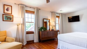 A bedroom with a bed, a dresser, a chair, a lamp, a TV, and two windows with curtains. - 5BR w/ 6 King Beds + Hot Tub (Louisville)