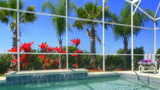 A swimming pool with clear water, surrounded by palm trees and red flowers, and a white structure in the background. - DISNEY AREA, Highlands Reserve SOUTH facing POOL, GAMES ROOM. SPECIALS AVAILABLE (Davenport)