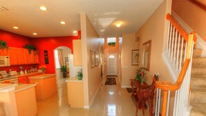 A spacious kitchen with a central island, a staircase with a wooden railing, and a hallway leading to a door. - DISNEY AREA, Highlands Reserve SOUTH facing POOL, GAMES ROOM. SPECIALS AVAILABLE (Davenport)