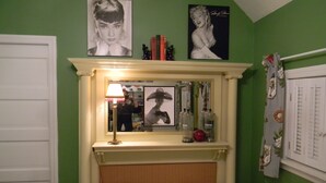 Een slaapkamer met een bed, een spiegel, een lamp en twee afbeeldingen in lijsten aan de muur.