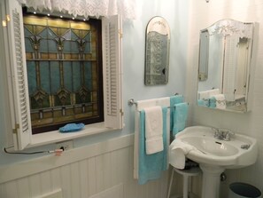 Une salle de bain avec un lavabo blanc, une fenêtre ornée de vitraux et un miroir décoré de motifs floraux.