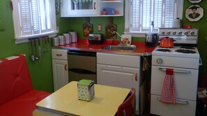 Een retro keuken met een rood-wit kleurenschema, oude apparaten en een klein zithoekje met een tafel en stoelen.