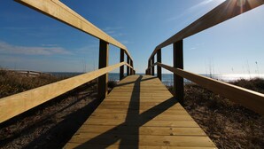 A wooden boardwalk leading to the beach with a clear sky and sun shining.