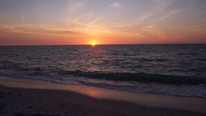 Ranta auringonlaskun aikaan, ja aurinko laskee meren taa.