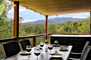 Eine Terrasse mit Esstisch und Stühlen, mit Blick auf eine gebirgige Landschaft.