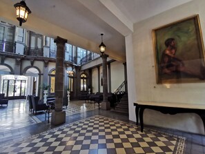 Een ruime lobby met een zwart-witte vloer, zuilen, een trap en een schilderij aan de muur.