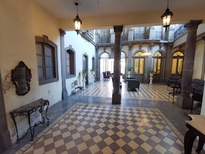 Een ruime lobby met geruit vloerkleed, versierde zuilen en klassiek meubilair.