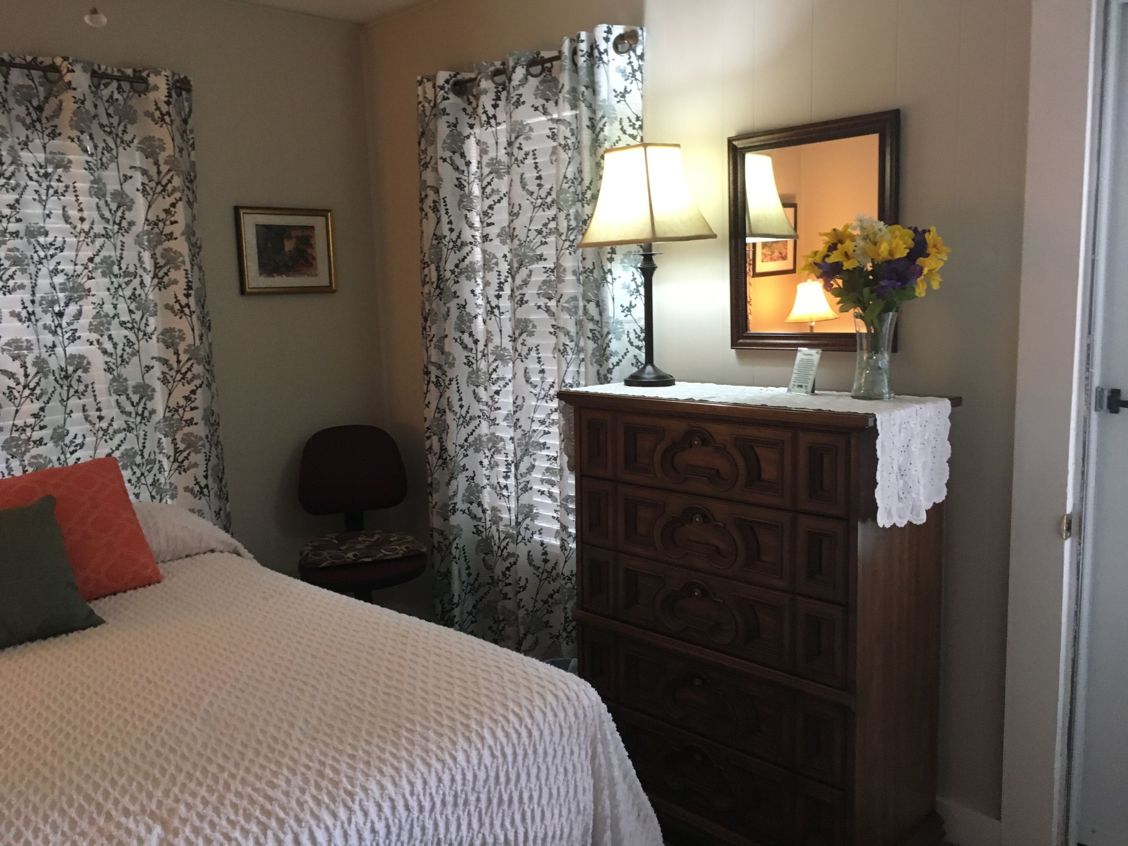 A bedroom with a bed, a dresser with a mirror, a lamp, and a vase with flowers.