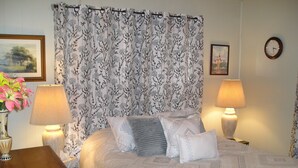 Une chambre à coucher bien rangée, avec un lit, deux lampes de chevet, une horloge et un rideau à motifs floraux.