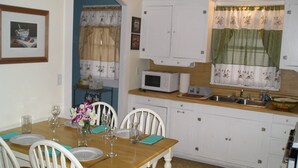 Un coin repas avec une table en bois dressée pour quatre personnes, des chaises blanches, un four à micro-ondes et un évier dans la cuisine.