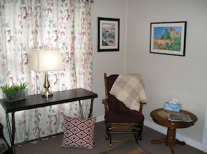 A living room with a table, chair, lamp, and two framed paintings on the wall.