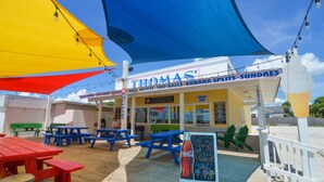 Un restaurant situé en bord de mer, appelé « THOMAS », avec une terrasse, un panneau publicitaire Coca-Cola et un tableau affichant le menu.