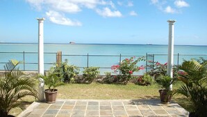 A view from a covered patio with a clear blue sky, a calm sea, and a distant ship.