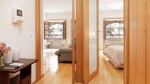 A bedroom with a wooden floor, a bed, a window with a view, and a bedside table with a lamp.