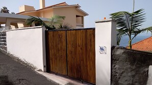 Una entrada con reja, una puerta de madera, un muro blanco y un letrero que indica 'AL' con un logotipo.