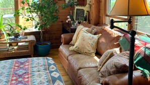A cozy cabin interior with a leather sofa, a patterned rug, a potted plant, and wooden walls. - Jaw-Dropping Coastal Mountain & Ocean View Post & Beam Log Getaway  (Rockport)