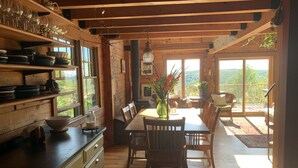 A rustic wooden interior with a dining area, wooden shelves with dishes, and a view through large windows. - Jaw-Dropping Coastal Mountain & Ocean View Post & Beam Log Getaway  (Rockport)