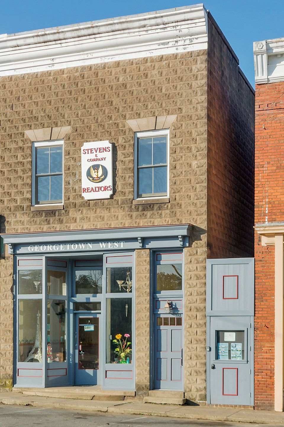 Een gebouw met twee verdiepingen, een gevel van baksteen, een bord van Stevens & Company Realtors en een etalage met grote ramen en een blauw luifel.