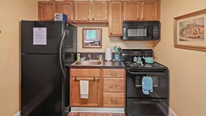 A compact kitchen with wooden cabinets, a black refrigerator, a microwave, and a stove. - Stay in Crozet Mountain Suite in Downtown Crozet (Crozet)