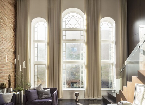A spacious room with large arched windows, a brick wall, a modern staircase, and a purple sofa.