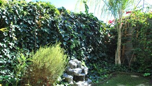 Um jardim com uma cascata de pedra, vegetação densa e um cercado de madeira.