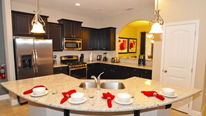 Una cocina moderna con armarios oscuros, electrodomésticos de acero inoxidable, una encimera de granito y una isla central con fregadero.