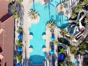 An aerial view of a resort with a central swimming pool, surrounded by palm trees and lounge chairs. - No Rear Neighbors • Pool & Spa • Game Room • Lazy River • Near Disney (Davenport)