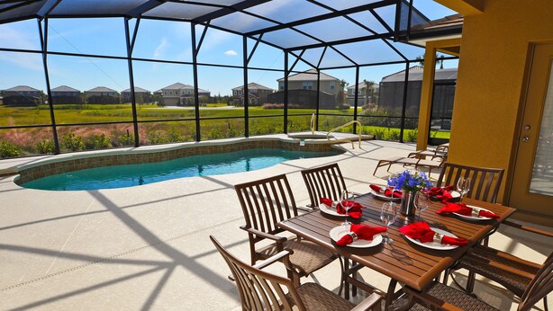Un espacio al aire libre techado con piscina, mesa de comedor lista para cuatro personas y sillas.