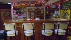 Eine Bar mit einer Theke, Stühlen und verschiedenen Dekorationen, darunter ein Schild mit der Aufschrift 'Seagram's Greetings' und einer Uhr.